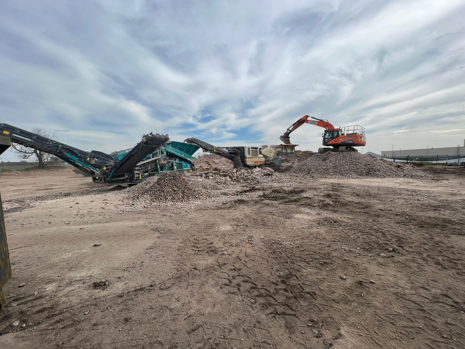 A large pile of dirt next to a concrete crushing machine at a construction site.