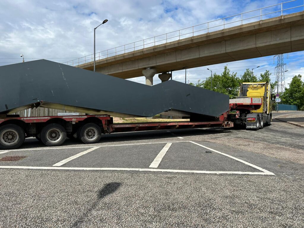 A semi truck hauling a large object, likely part of a dismantling project, drives down the highway.
