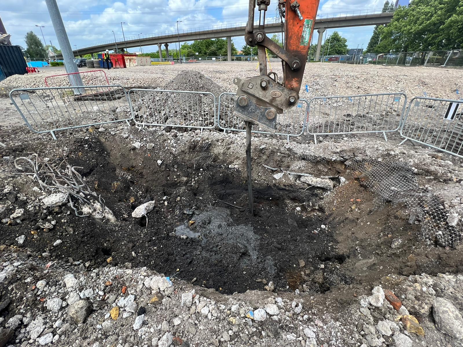 A large hole in the ground, part of enabling works, showing excavation and surrounding dirt.