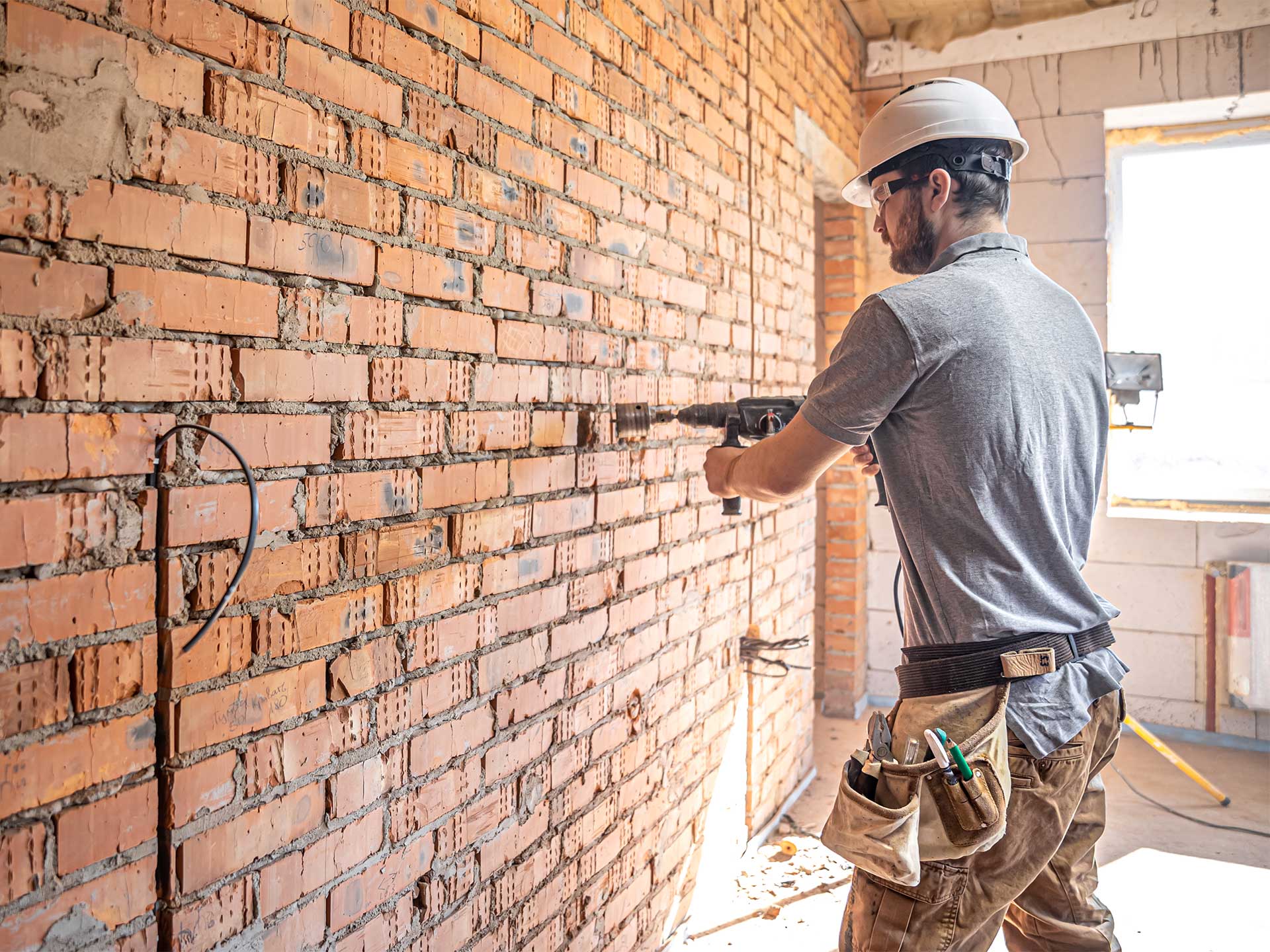 A man is making structural alterations to a brick wall, focused on his work with tools in hand.